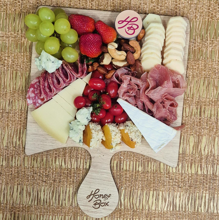 Mãos montando uma cesta de presentes gourmet com frutas e queijos.